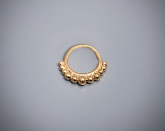 May include: Gold hoop nose ring with a beaded design. The ring is made of metal and has a smooth finish.