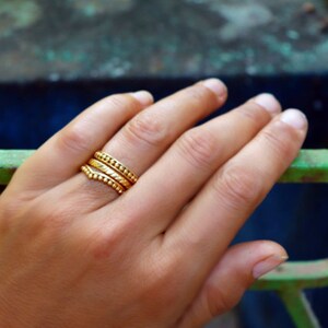 May include: A hand wearing three gold stacking rings with textured surfaces. The rings are worn on the ring finger.