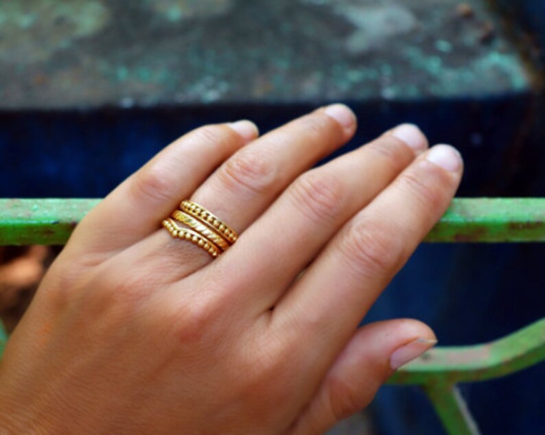 May include: A hand wearing three gold stacking rings with textured surfaces. The rings are worn on the ring finger.