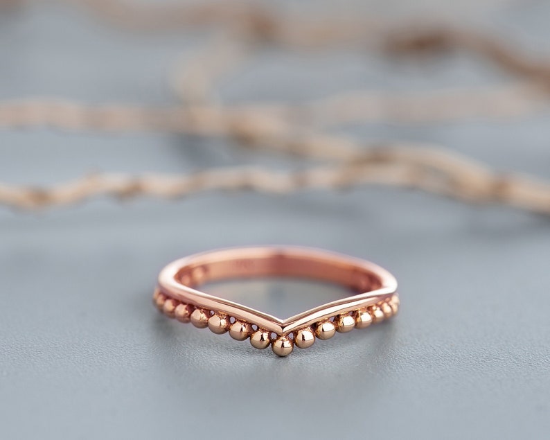 May include: A rose gold ring with a V-shaped band and a row of small beads along the edge.