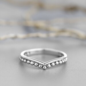 May include: A silver ring with a V-shaped band and a row of small beads along the edge.