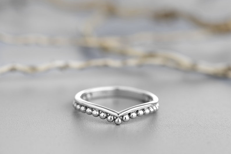 May include: A silver ring with a V-shaped band and a row of small beads along the edge.