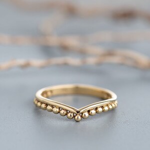 May include: A gold band ring with a V-shaped design and a row of small beads along the edge.