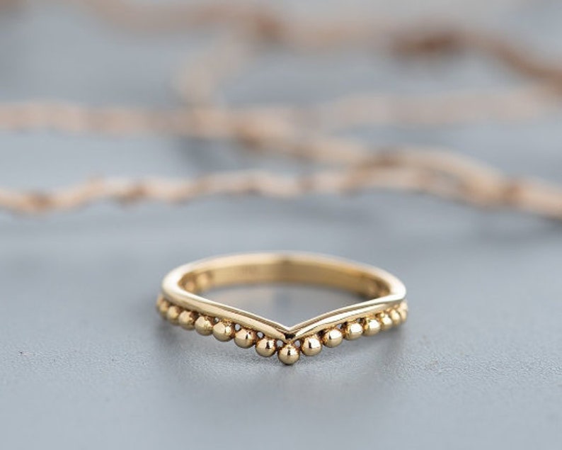 May include: A gold band ring with a V-shaped design and a row of small beads along the edge.