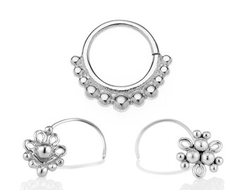 Könnte beinhalten: Drei silberne Nasenringe. Der obere Ring ist ein Reifen mit einer Reihe kleiner Perlen. Die beiden unteren Ringe sind gebogen mit einem blütenförmigen Design.