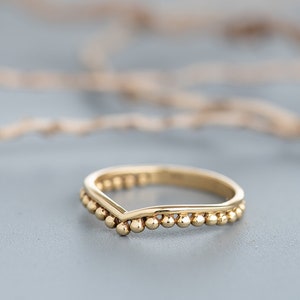 May include: A gold-colored ring with a V-shaped band and a beaded edge.