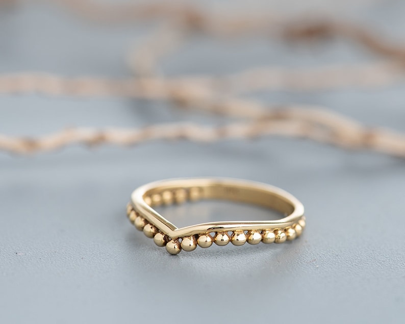 May include: A gold-colored ring with a V-shaped band and a beaded edge.