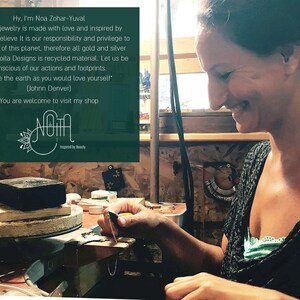 May include: A woman working on jewelry in her workshop. She is using a small tool to shape a piece of metal. The text on the wall reads "Hy, I'm Noa Zohar-Yuval. All my jewelry is made with love and inspired by beauty. I believe It is our responsibility and privilege to take care of this planet, therefore all gold and silver used by Noita Designs is recycled material. Let us be conscious of our actions and footprints. 'love the earth as you would love yourself' (Johnn Denver) You are welcome to visit my shop Noita Inspired by Beauty."