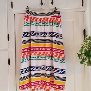 May include: A white skirt with colorful horizontal stripes and geometric patterns. The skirt has a black waistband and a gathered waist.