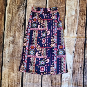 May include: A long, navy blue skirt with a colorful geometric and floral print. The skirt has a high waist and a flowy silhouette.