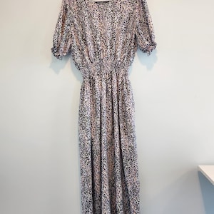 May include: A white maxi dress with a black and pink abstract print. The dress has a fitted bodice and a flowy skirt. The dress has short puff sleeves with ruffles at the cuffs. The dress has a smocked waist.