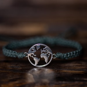 May include: A dark green braided bracelet with a silver charm in the shape of the world.