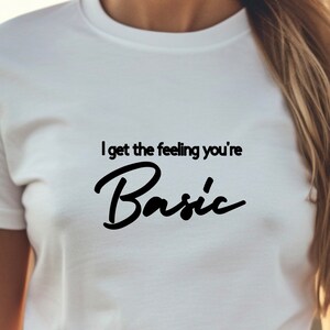 以下が含まれることがあります： 「I get the feeling you're Basic」という黒い文字が書かれた白いTシャツ。