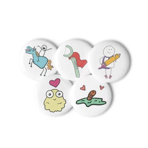 May include: Five white round buttons with colorful cartoon illustrations. The buttons feature a stick figure riding a unicorn, a dental floss with a cape, a stick figure holding a pencil, a yellow blob with a heart, and a worm in the grass.