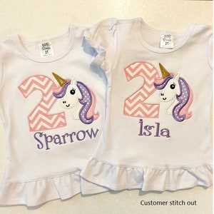 May include: Two white t-shirts with pink and white chevron number 2 and a unicorn with a gold horn, purple mane, and pink ears. One shirt says "Sparrow" and the other says "Isla".