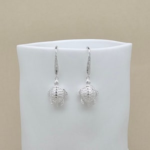 Peut inclure: Une paire de boucles d'oreilles pendantes en argent avec un motif de tortue détaillé. Les boucles d'oreilles sont en argent sterling et ont une finition polie.