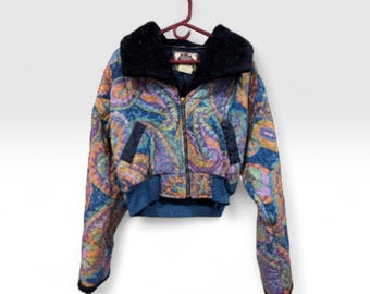 May include: A cropped jacket with a vibrant paisley pattern in blue, purple, orange, and yellow. The jacket features a black faux fur collar, a zip closure, and dark blue detailing. It is suspended from a red hanger.