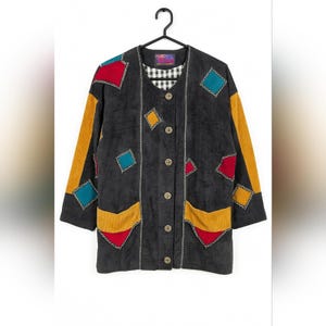 Peut inclure: Veste en velours côtelé noir avec des patchs géométriques colorés rouges, jaunes et turquoise. La veste a une doublure à carreaux, une fermeture boutonnée et deux poches avant. Les manches ont des rayures en velours côtelé jaune.