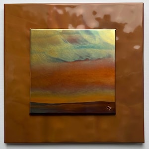 May include: A square metal wall art piece featuring a glossy, textured copper-colored border surrounding a central panel. The center panel displays a landscape scene with a gradient of blue, orange, and yellow hues, signed with the initials SVY.