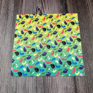 May include: A square fabric swatch with a repeating pattern of colorful cartoon-like creatures and leaves. The background transitions from green to blue. The creatures are in various colors, including purple, red, and yellow.