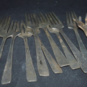 May include: A collection of silver forks with ornate designs. The forks are arranged in a pile, with the tines pointing in different directions.