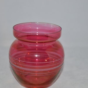 May include: A small, pink glass vase with white stripes. The vase has a rounded body and a wide mouth.