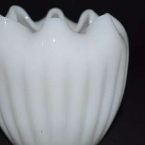 May include: A white milk glass bud vase with a fluted design and a scalloped rim.
