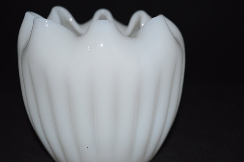 May include: A white milk glass bud vase with a fluted design and a scalloped rim.