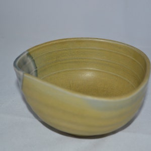 May include: A small, yellow ceramic bowl with a slightly uneven rim. The bowl has a subtle, striped pattern and a light gray glaze.
