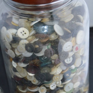 May include: A glass jar filled with a variety of buttons in different colors, shapes, and sizes. The jar has a wooden lid.