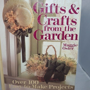 May include: Book cover with a title that reads "Gifts & Crafts from the Garden" by Maggie Oster. The cover features a straw hat with a green ribbon and a wicker basket filled with dried flowers and a green ribbon.