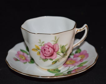May include: A white teacup and saucer with a gold trim and a pink rose floral design.