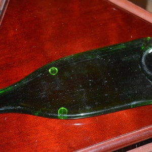 May include: A green glass bottle that has been cut and smoothed to create a serving tray. The tray is sitting on a dark wood surface.