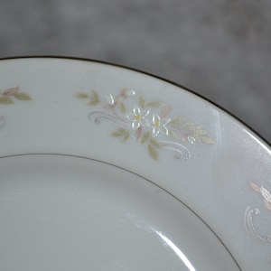 Puede incluir: Un plato de cerámica blanco con un borde dorado y un delicado diseño floral en tonos de rosa y verde.