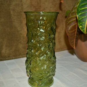 May include: A green glass vase with a textured surface. The vase is tall and slender with a round base.