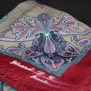 May include: A red and beige silk scarf with a paisley pattern and the text "Gerard P. Paris" in the bottom right corner.