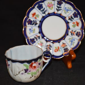 May include: A white teacup and saucer with a blue and gold floral design. The cup has a scalloped rim and the saucer has a scalloped edge.