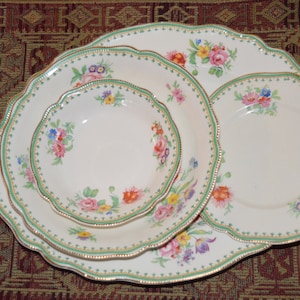May include: A set of vintage porcelain dishes with a floral pattern. The set includes a large platter, a plate, and a bowl. The edges are scalloped and trimmed with gold and green. The floral design features pink, yellow, blue, and orange flowers.