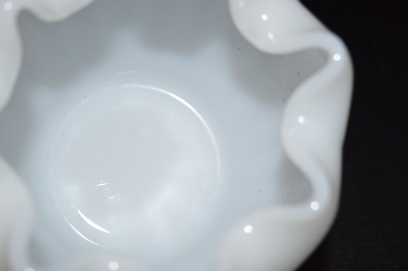 May include: A white ceramic bowl with a ruffled edge. The bowl is empty and has a smooth, glossy finish.