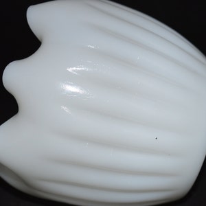 May include: A white milk glass vase with a fluted design. The vase has a rounded bottom and a wide opening.