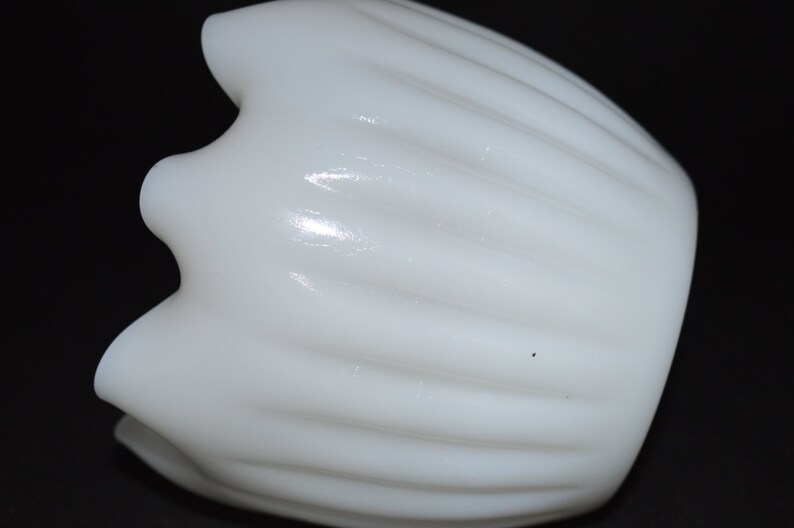 May include: A white milk glass vase with a fluted design. The vase has a rounded bottom and a wide opening.
