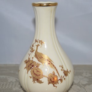 May include: A white ceramic vase with a gold rim and a gold and brown floral design featuring a bird.