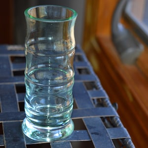 May include: A clear glass shot glass with a textured, ribbed design. The glass has a light green tint and a rounded base.