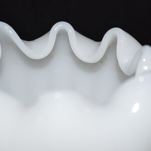 May include: White milk glass bowl with a scalloped edge. The bowl is made of opaque white glass and has a smooth, glossy finish.