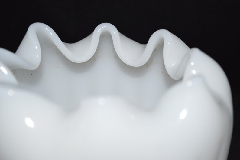 May include: White milk glass bowl with a scalloped edge. The bowl is made of opaque white glass and has a smooth, glossy finish.