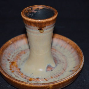 May include: A ceramic ring holder with a brown and white glaze. The holder has a tall, cylindrical base and a wide, flat top.