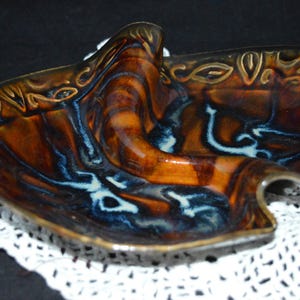 Puede incluir: Un plato de servir de cerámica con un diseño abstracto único. El plato es marrón, azul y blanco con un acabado brillante. Tiene una forma ondulada y orgánica.