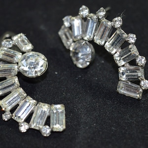 Puede incluir: Un par de pendientes de plata con forma de media luna, adornados con brillantes transparentes. Los pendientes presentan un gran brillante redondo en el centro de cada media luna.