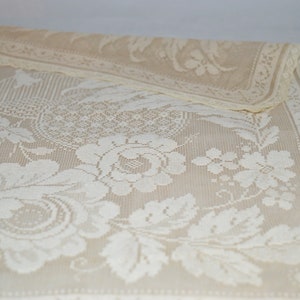 Puede incluir: Un camino de mesa de crochet blanco con un diseño floral. El camino de mesa presenta una rosa grande con hojas y flores más pequeñas.