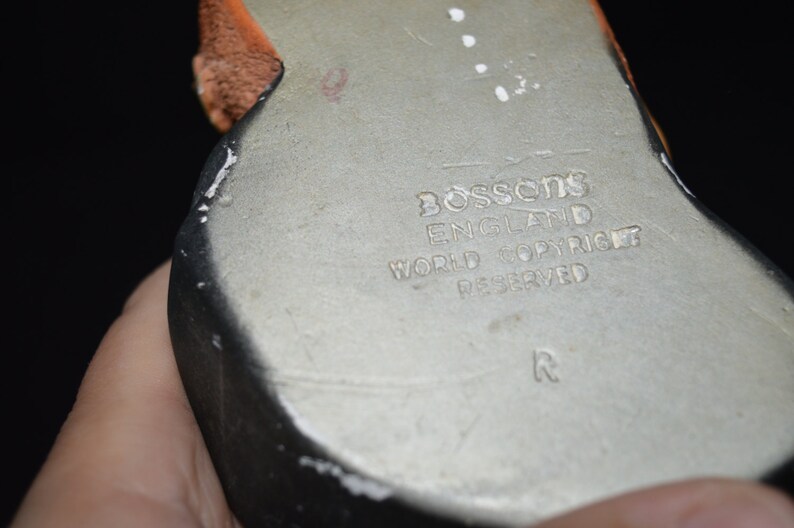 Puede incluir: Primer plano de la parte inferior de una figurita de cer&aacute;mica. La parte inferior es plateada con un borde negro y el texto "Bossons England World Copyright Reserved R" est&aacute; impreso en la parte inferior.